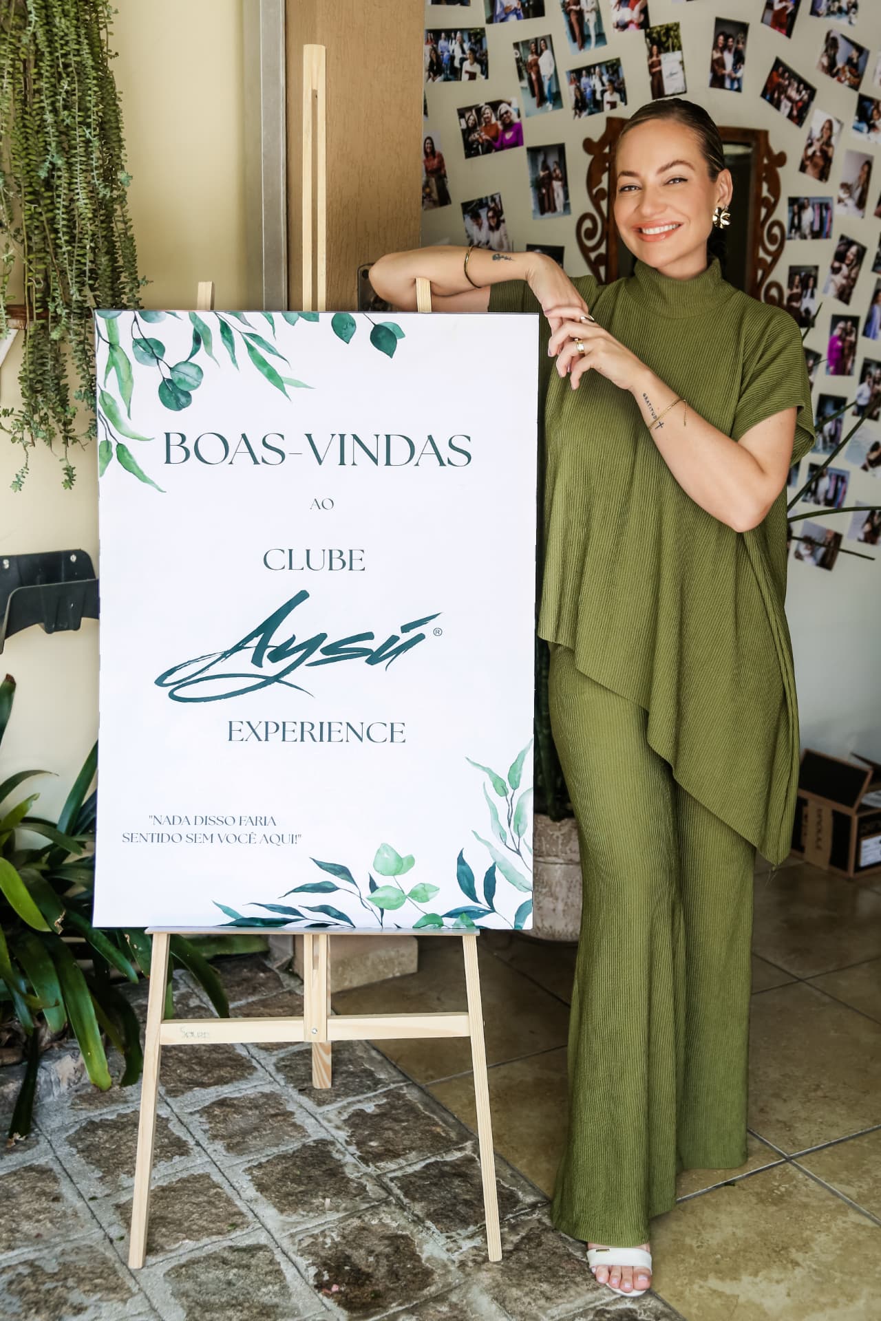 Dra. Maikiara ao lado do painel de boas-vindas do Clube Aysú Experience